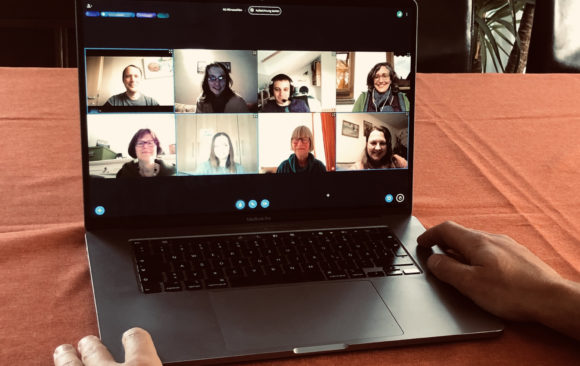 Laptop auf Tisch, auf dem eine Videokonferenz mit 8 Personen zu sehen ist