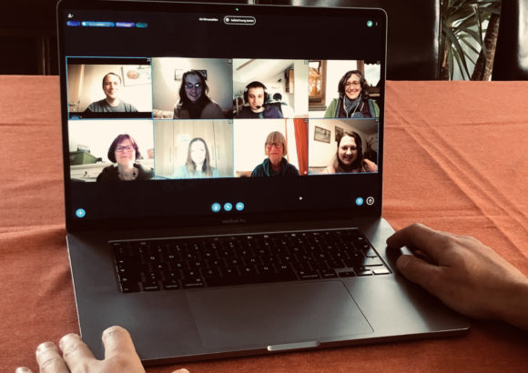 Laptop auf Tisch, auf dem eine Videokonferenz mit 8 Personen zu sehen ist