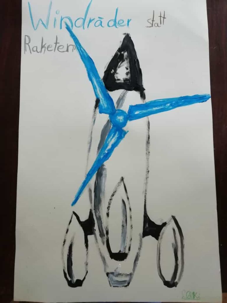 Kinderzeichnung mit einer Rakete, an der sich blaue Windrad-Flügel drehen. Handschriftlich "Windräder statt Raketen"